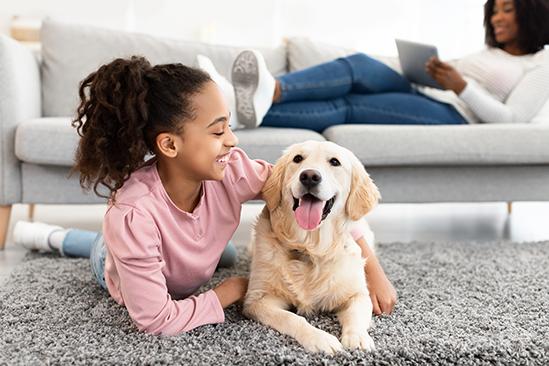 A girl smiling and lying on the floor with her arm around her happy dog.